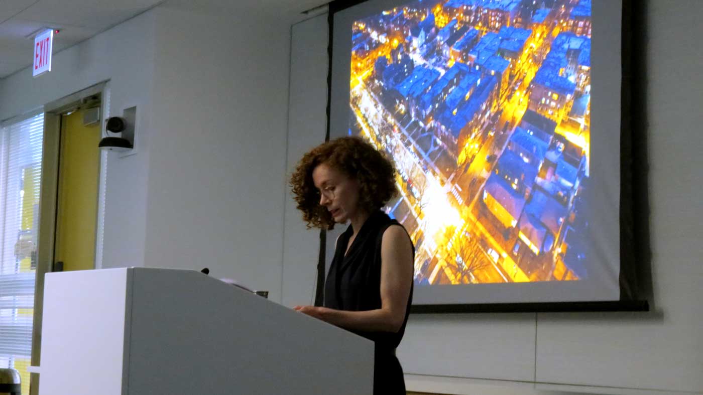 A presenter stands at a podium with an image projected behind them