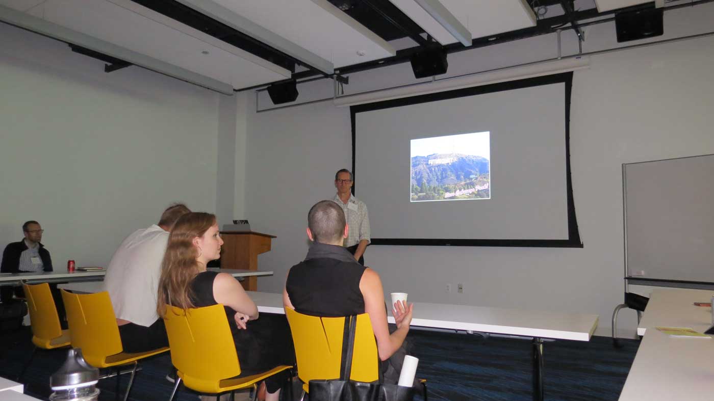 people sit and look at a powerpoint from a presenter in the front of the room