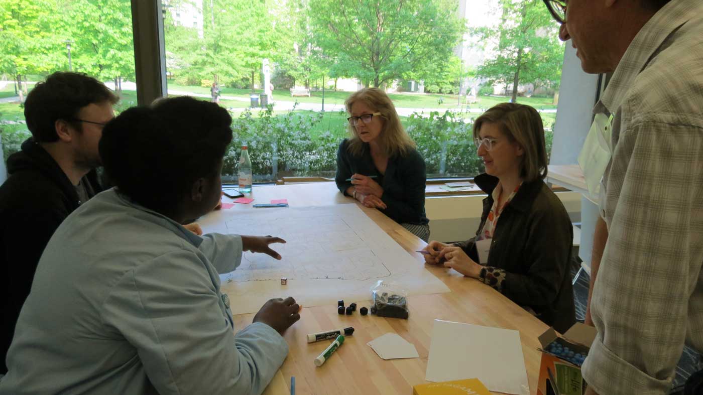 five people sit or stand around a table focused on a large piece of paper