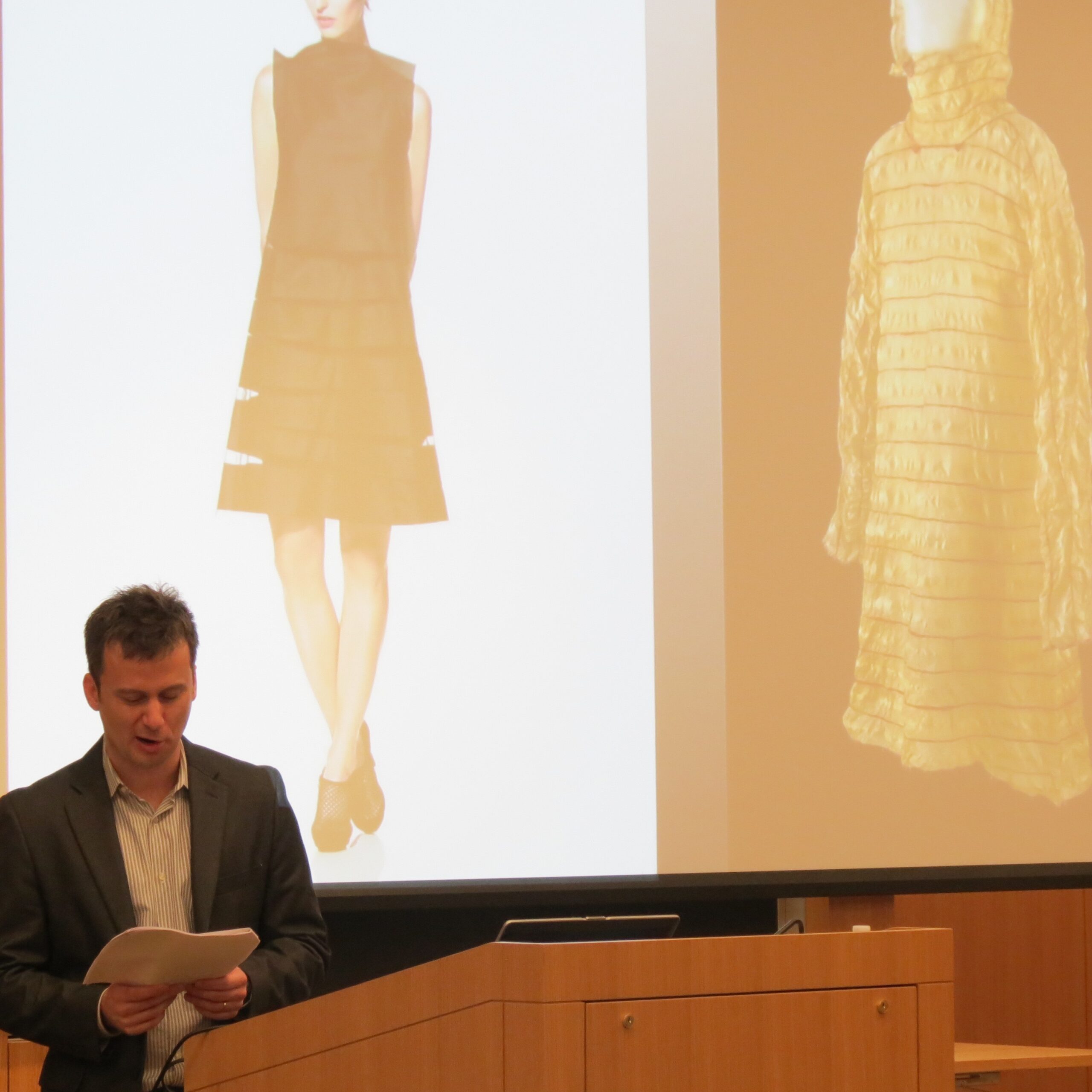 speaker reading aloud in front of slide of two dresses on mannequins