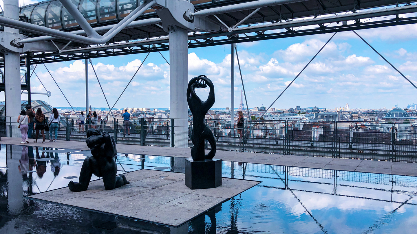 view from the top of the Centre Pompidou in Paris; with sculptures, reflecting pool, passersby, and skyline