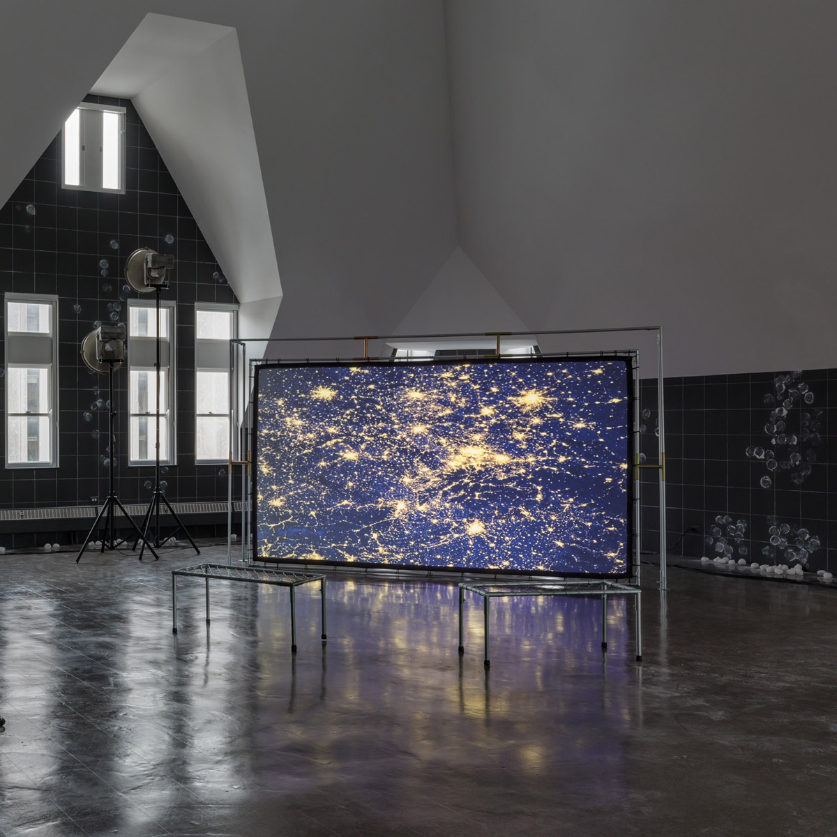 a large screen with birds-eye view of city lights sits within a large gallery space
