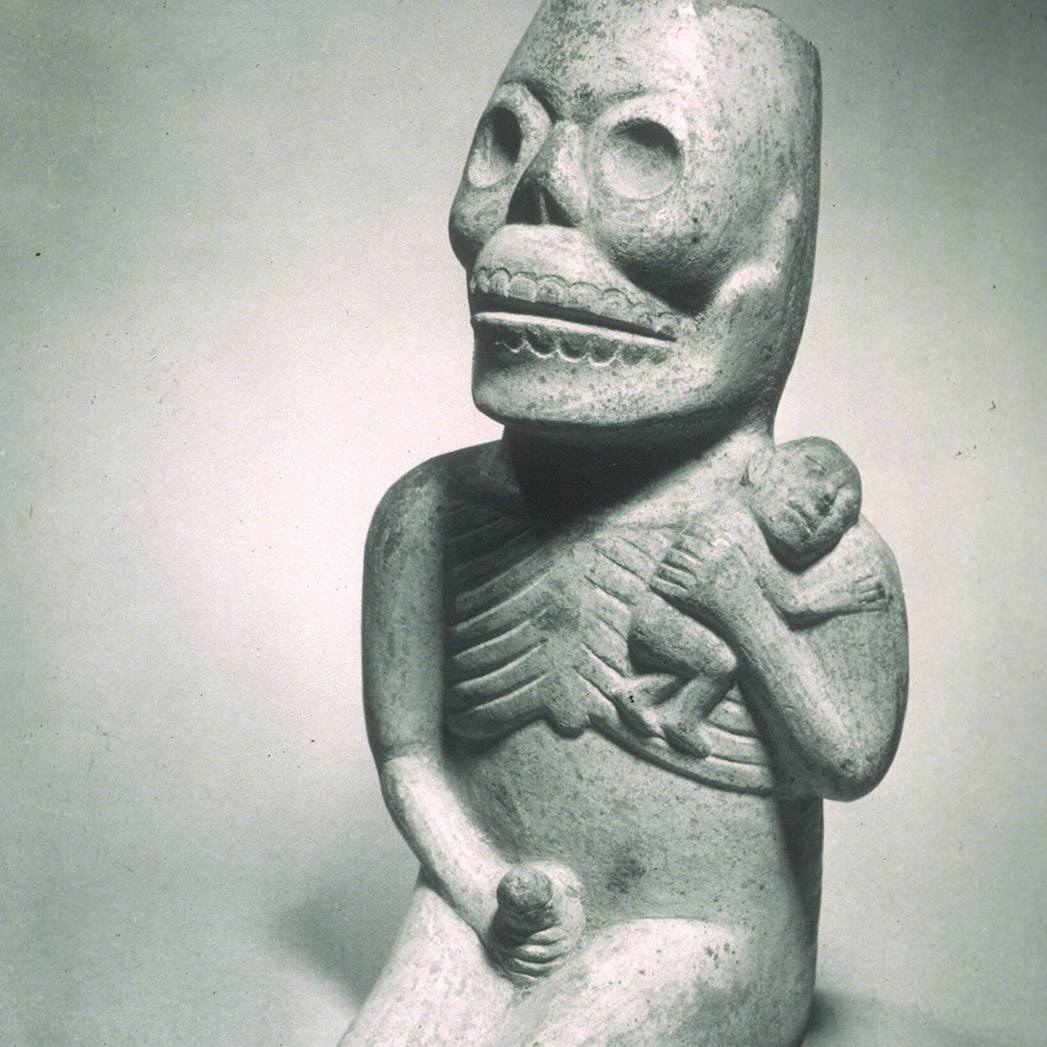 photograph of an ancient Peruvian sculpture in gray stone of a kneeling figure holding an infant