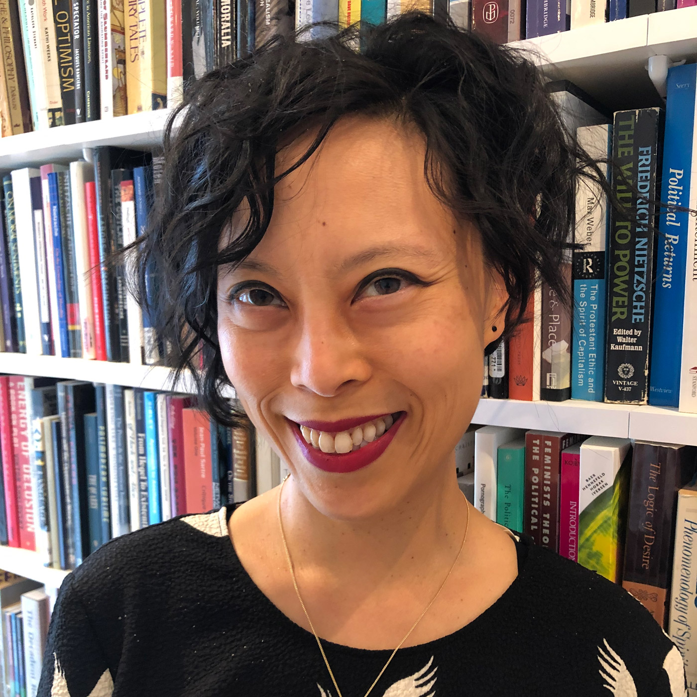 portrait of Sianne Ngai smiling and standing in front of a bookshelf