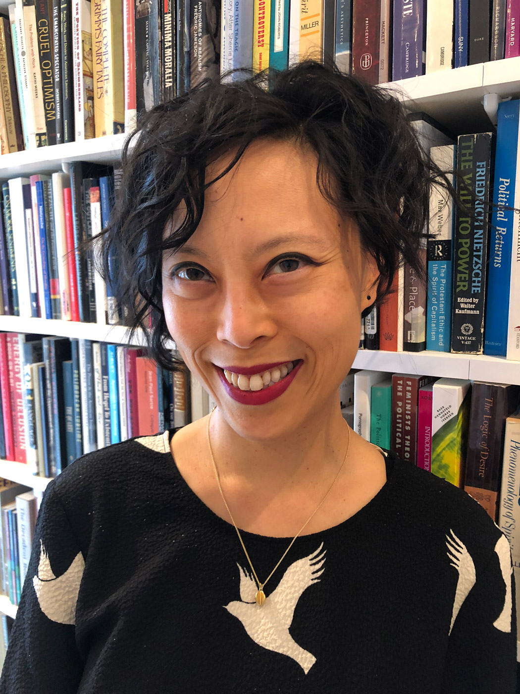 portrait of Sianne Ngai smiling and standing in front of a bookshelf