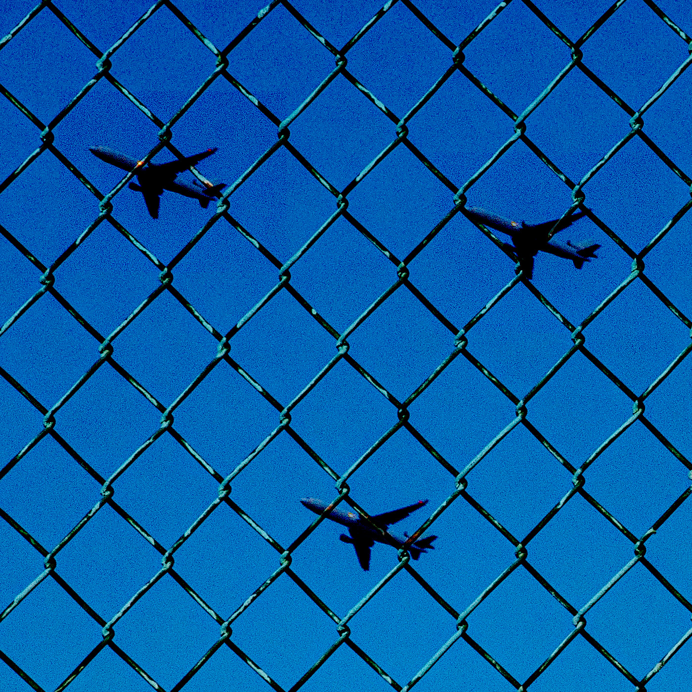 three airplanes against a blue sky overlaid with a chain link fence