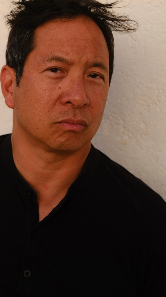 Head and upper torso of person wearing black shirt standing in front of textured cream wall