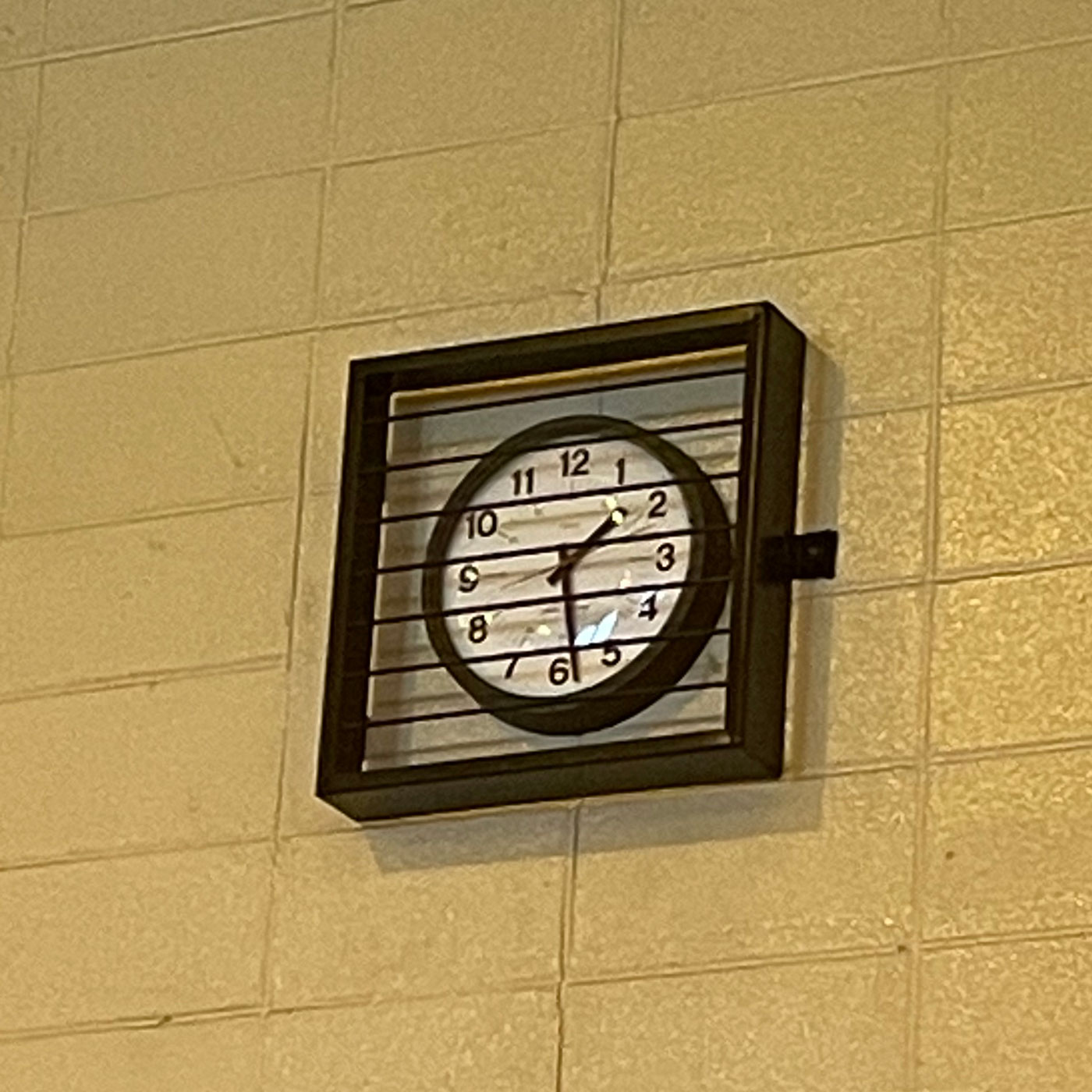 clock mounted on a yellow cinder block wall covered with a protective grid